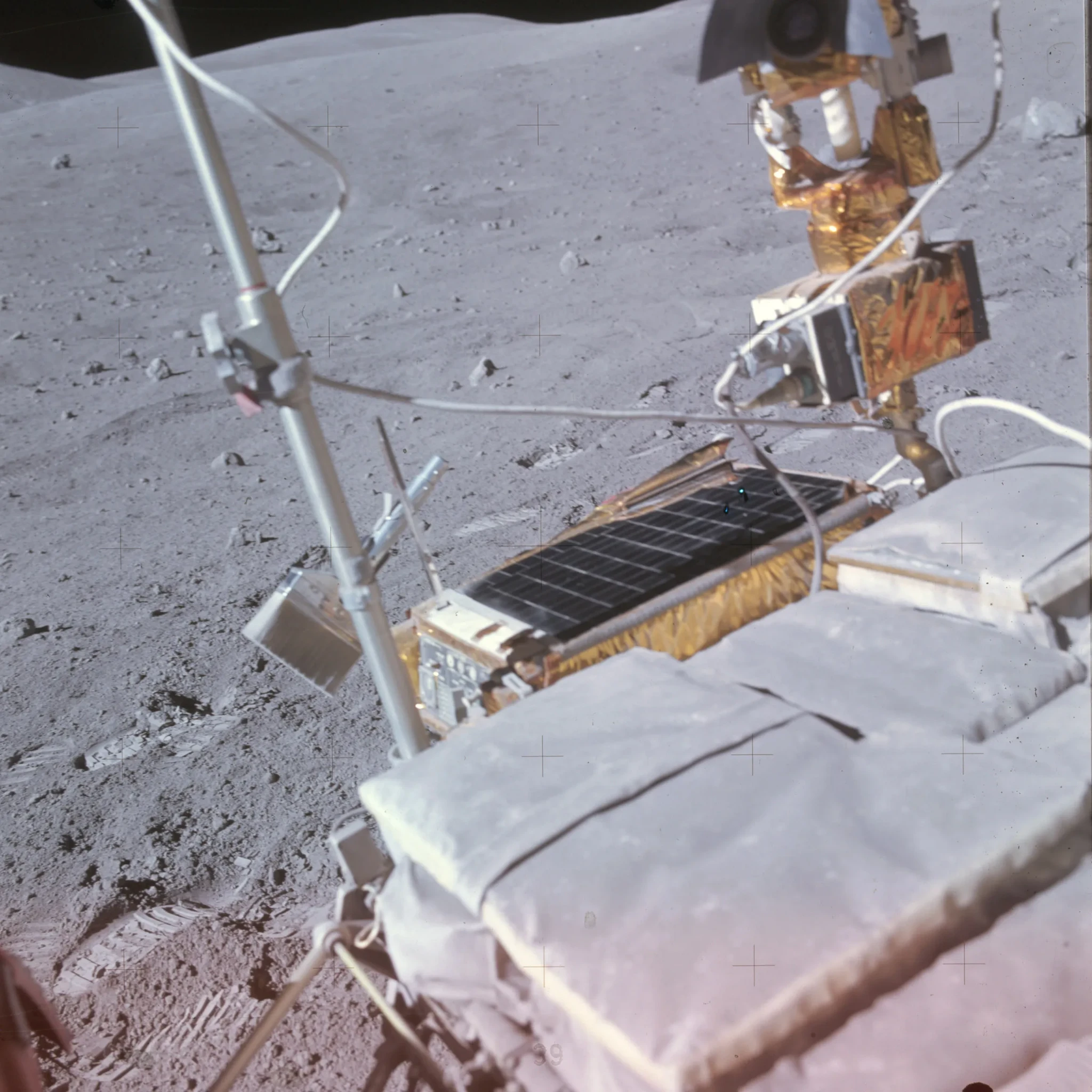 A color photograph of the Apollo 16 lunar rover, centering on some equipment. The object in focus at the center left is a dust brush. Footprints can be seen on the lunar surface behind the rover near the tool’s attachment point, implying the dust brush was recently in use. https://www.nasa.gov/history/alsj/picture.html