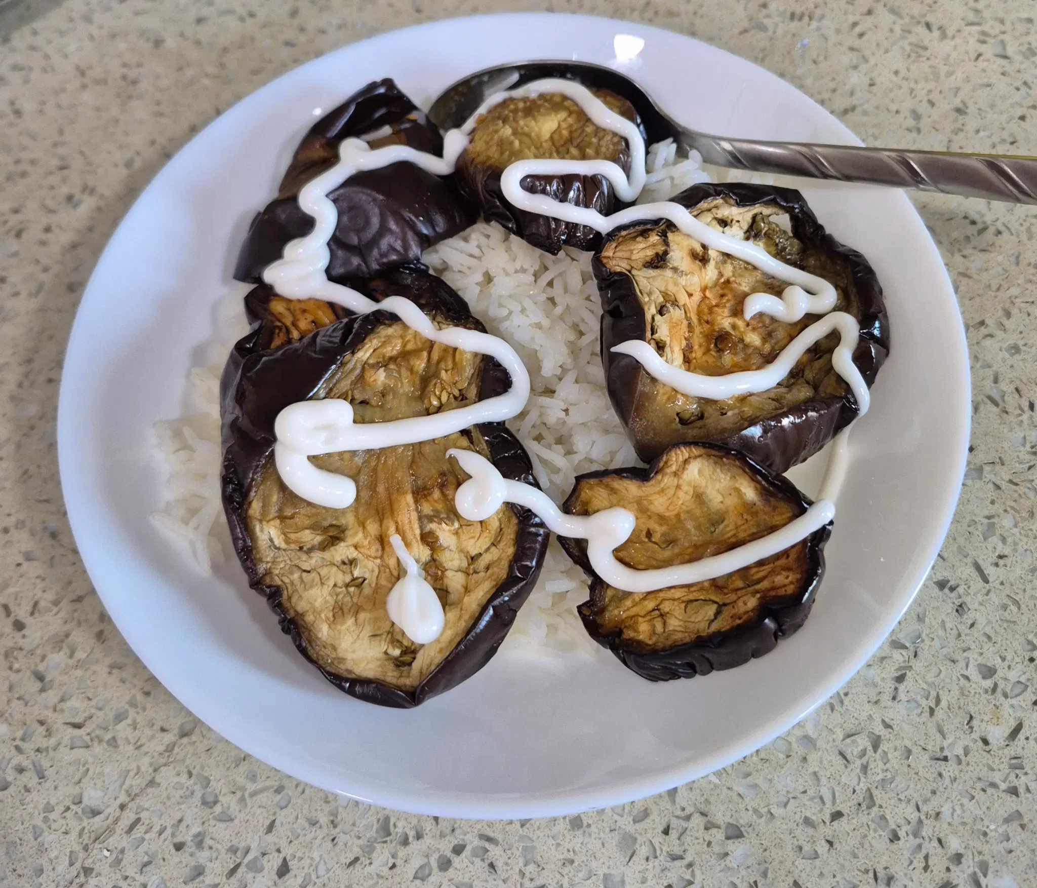 a plate of rice, fried eggplants, and mayonnaise. There's also a spoon.